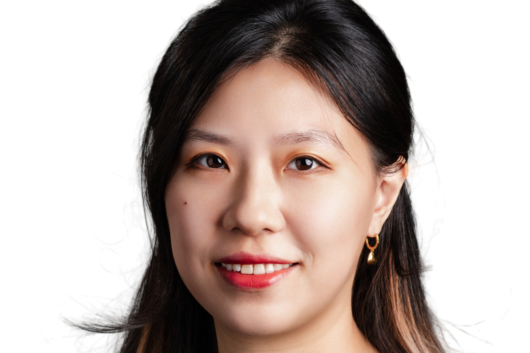 Vestacon_07302025_R1 -6_(2) Smiling woman with shoulder-length dark hair, wearing pearl earrings and a black top, against a gray background.